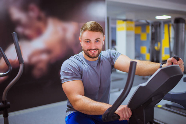 Smiling happy man does exercises on simulator at the gym - Photo, image