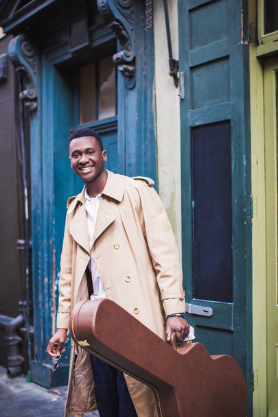Portrait of young happy smiling man who stands with guitar case in hand, outdoor - Foto, Bild