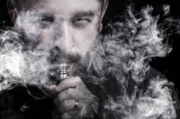man on black background close-up with vape in mouth surrounded by smoke - Photo, Image