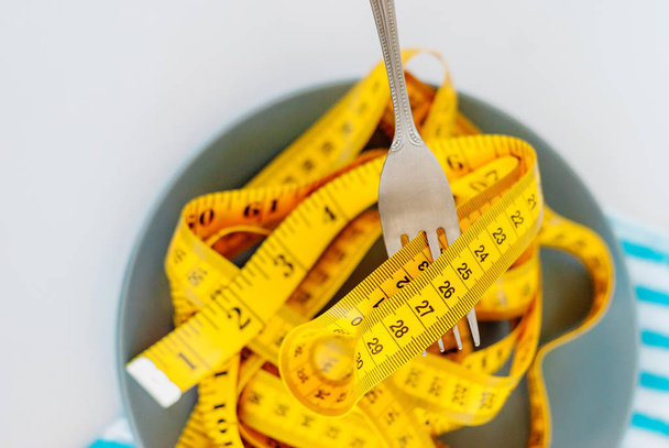 The concept of the diet. The fork rewound centimeter lying on plate - 写真・画像