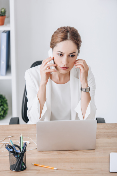 stressed businesswoman talking on smartphone at workplace with laptop  - Zdjęcie, obraz