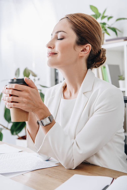 attractive businesswoman rest with closed eyes and holding coffee to go in office on coffee break - Foto, afbeelding