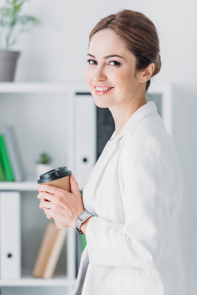 attractive cheerful businesswoman with coffee to go in modern office - Photo, Image