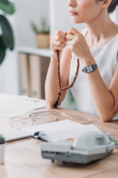 cropped view of businesswoman praying with rosary beads in modern office - Photo, Image