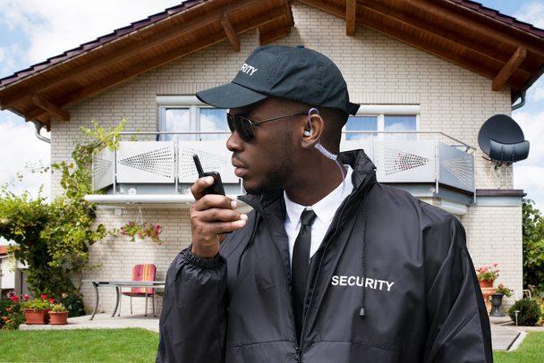 Young African Male Security Guard Talking On Walkie Talkie In Front Of House - Фото, зображення