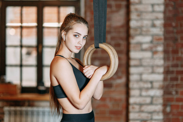 Sports girl doing stretching in the gym with rings Stands and smiles, holding on to the rings, rest in training. Professional equipment and clothing - Fotó, kép