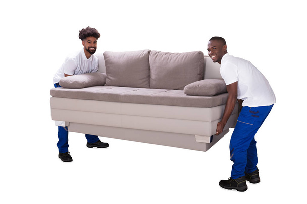 Two Smiling African Male Movers Moving Sofa On White Background - Фото, зображення