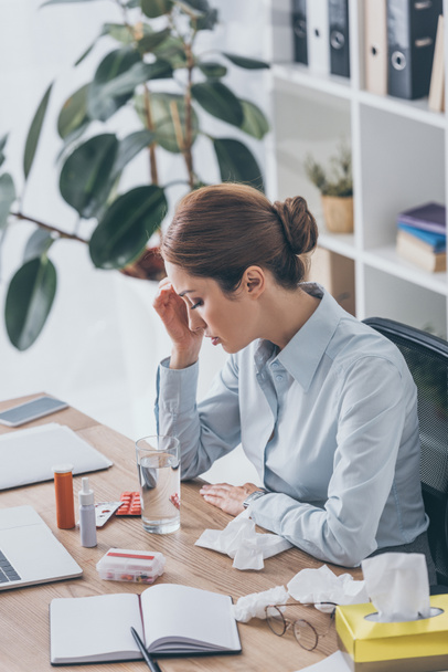 depressed sick businesswoman sitting at workplace with various medicines - Photo, Image