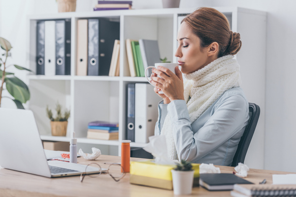 close-up portrait of ill businesswoman in scarf drinking hot tea at office - Photo, Image