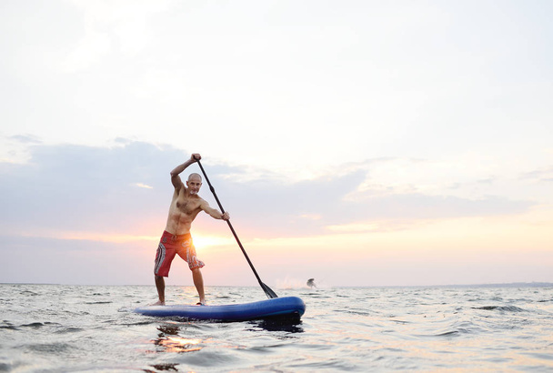 A man stands on a SUP board against the background of the sea - Foto, Imagen