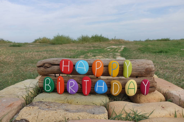 Gelukkige verjaardag samenstelling met gekleurde stenen op bossen en bakstenen met natuur achtergrond - Foto, afbeelding