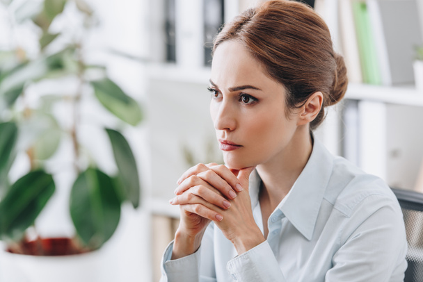 close-up portrait of serious businesswoman sitting at workplace and looking away - Фото, изображение