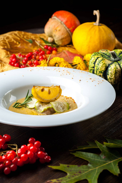 Pumpkin cream soup with fish som. A dish at a restaurant for Halloween celebrations. Black background, brick wall and wooden table - Photo, image