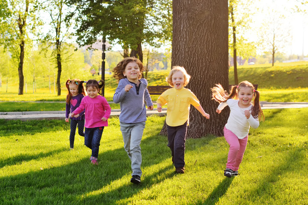 een groep van kleine gelukkige kinderen lopen door het park in de achtergrond van gras en bomen.  - Foto, afbeelding