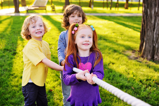 Grupa małych dzieci w wieku przedszkolnym grać przeciąganie liny w parku.  - Zdjęcie, obraz