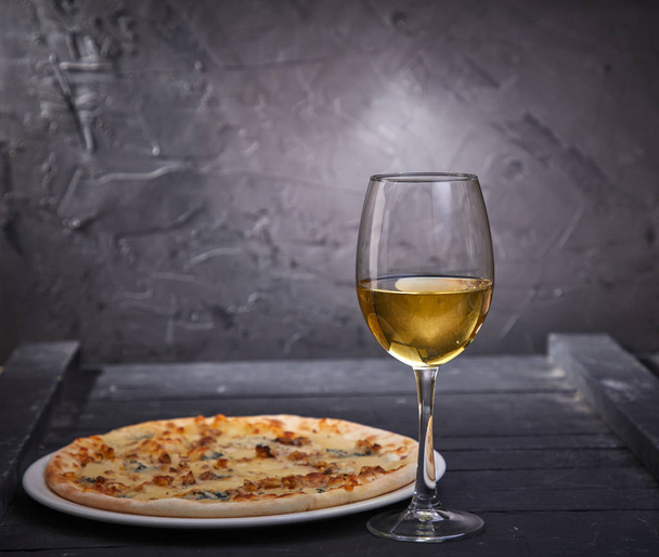 wineglass with cold white wine and pizza on grey background, close-up   - 写真・画像