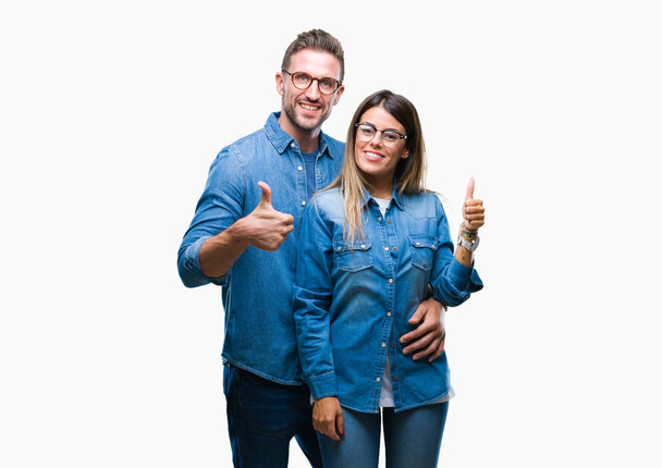 Young couple in love wearing glasses over isolated background doing happy thumbs up gesture with hand. Approving expression looking at the camera with showing success. - Photo, Image