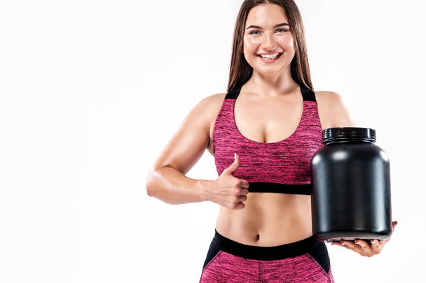 Happy and healthy muscular young fitness sports woman athlete with a jar of sports nutrition - protein, gainer and casein - Fotografie, Obrázek