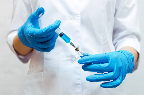 Jeringa con un medicamento médico azul en las manos del médico vestido con la bata médica
. - Foto, Imagen