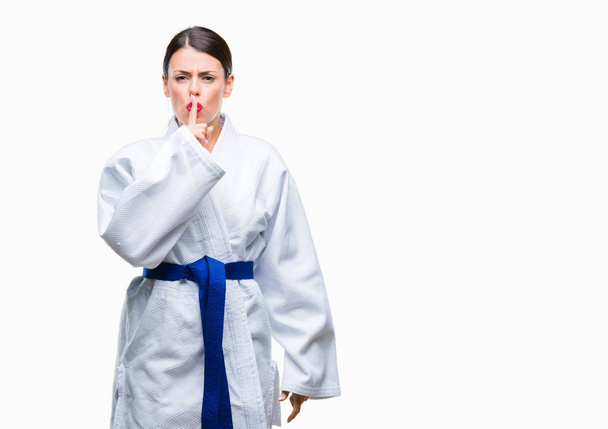 Dudaklarında parmak ile sessiz olmanı izole arka plan üzerinde karate kimono üniforma giyen genç güzel kadın. Sessizlik ve gizli kavramı. - Fotoğraf, Görsel