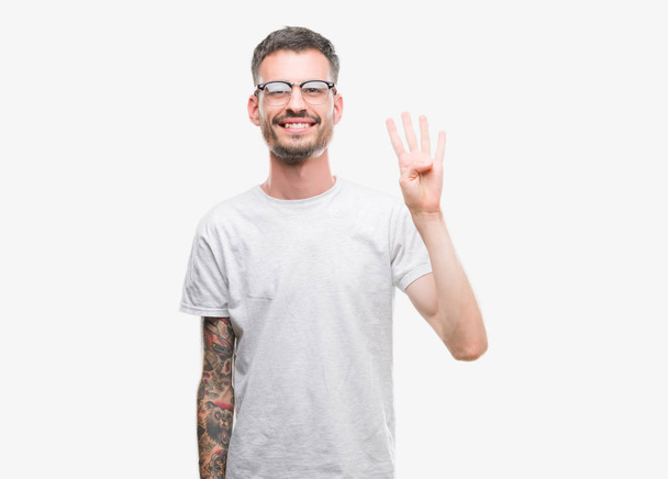 Jeune homme adulte tatoué montrant et pointant vers le haut avec les doigts numéro quatre tout en souriant confiant et heureux
. - Photo, image