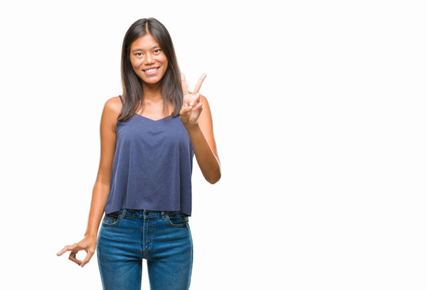 Młoda Azjatka kobieta na białym tle uśmiechnięty z szczęśliwy twarz mrugając aparat robi znak zwycięstwa. Numer dwa. - Zdjęcie, obraz