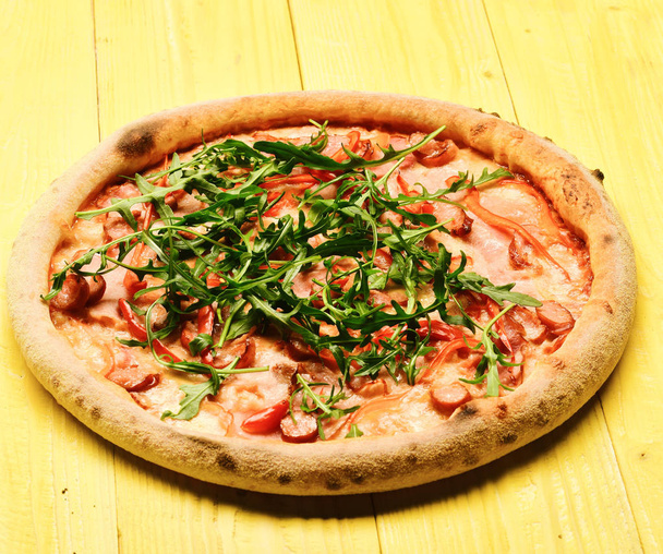 Pizza szalonnával, sajttal és arugulával, fa sárga alapon - Fotó, kép