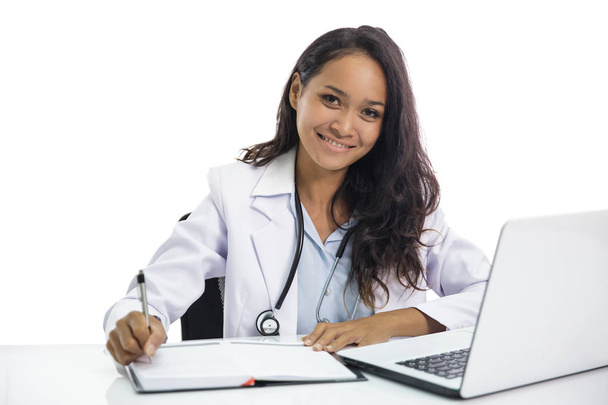 portrait of beautiful young doctor working on her laptop and writing on notebook isolated on white background - Foto, Imagen