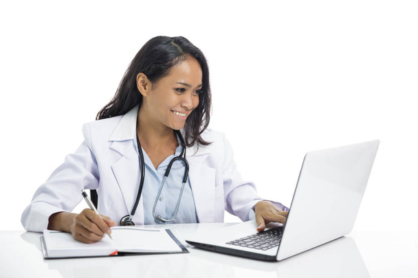 beautiful young doctor working on her laptop and writing on note - Фото, изображение