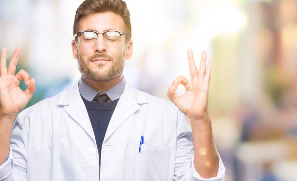 Young handsome man wearing doctor, scientis coat over isolated background relax and smiling with eyes closed doing meditation gesture with fingers. Yoga concept. - Photo, Image