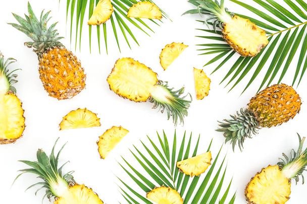 tropisches Nahrungsmuster aus Ananasfrüchten mit Palmblättern auf weißem Hintergrund. flache Lage, Draufsicht. - Foto, Bild