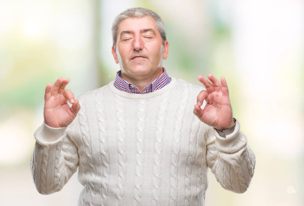 Hombre mayor guapo con suéter de invierno sobre fondo aislado relajarse y sonreír con los ojos cerrados haciendo gesto de meditación con los dedos. Concepto de yoga
. - Foto, Imagen