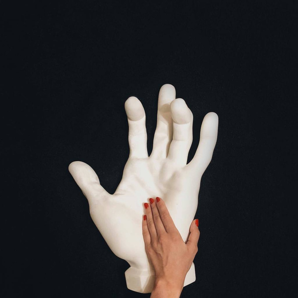 cropped image of female hand touching white hand sculpture against black background - Photo, image