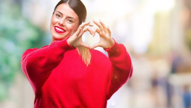 Young beautiful business woman wearing winter sweater over isolated background smiling in love showing heart symbol and shape with hands. Romantic concept. - Photo, Image