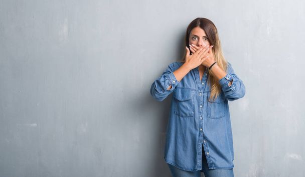 Mladé dospělé ženy grunge šedá zeď na sobě Džínové Oblečení šokován, pokrývající ústa rukama za chybu. Tajné koncept. - Fotografie, Obrázek