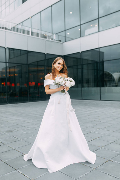Modern, stylish bride in European dress. Photo shoot on the street near the hotel. Bouquet and strict dress - Foto, Imagem