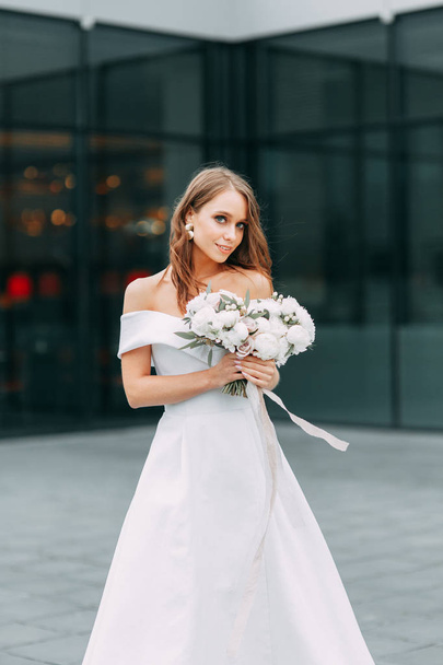 Modern, stylish bride in European dress. Photo shoot on the street near the hotel. Bouquet and strict dress - Фото, зображення