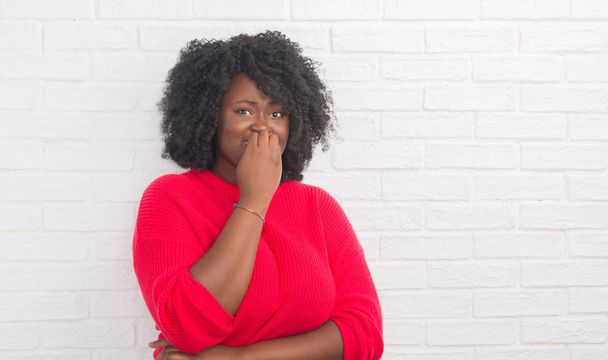 junge afrikanisch-amerikanische Plus-Size-Frau über der weißen Ziegelwand, die gestresst und nervös aussieht, die Hände auf den Mund beißenden Nägeln. Angstproblem. - Foto, Bild