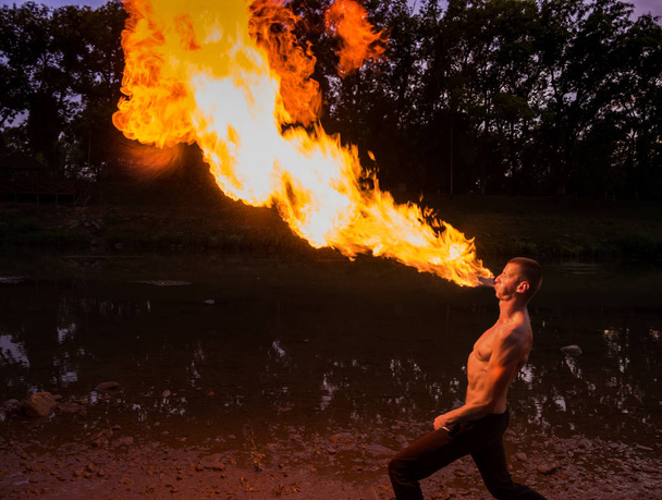  Hombre devorador de fuego soplando una gran llama de su boca
 - Foto, Imagen