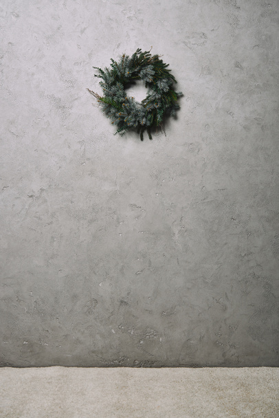 grüner Tannenkranz zur Weihnachtsdekoration hängt an grauer Wand im Zimmer - Foto, Bild