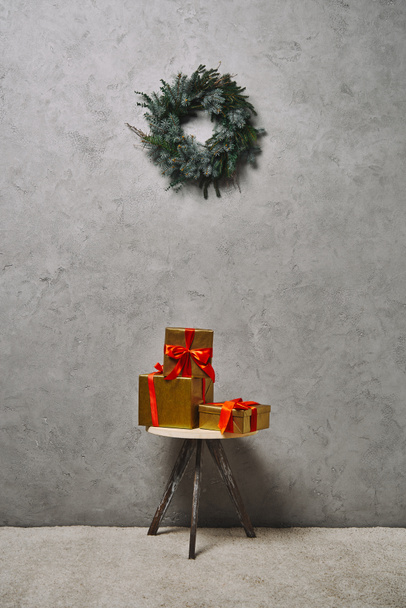 golden Christmas gift boxes with red ribbons on chair under fir wreath in room - Photo, Image