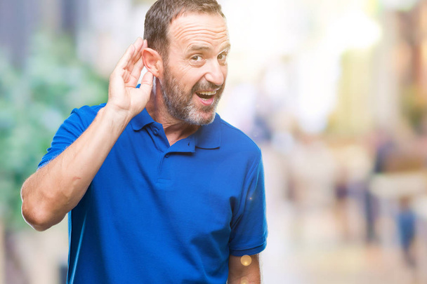Hombre mayor de mediana edad sobre un fondo aislado sonriendo con la mano sobre el oído escuchando un rumor o chismes. Concepto de sordera
. - Foto, imagen