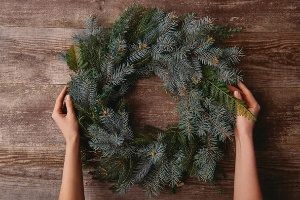 cropped image of woman holding christmas fir wreath at wooden table - Photo, Image