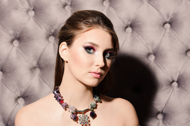 Girl wearing colourful makeup and necklace on grey leather background - Foto, imagen