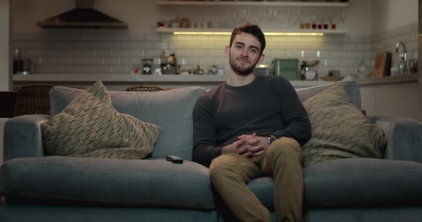 junger Mann entspannt auf einer Couch vor dem Fernseher, lächelt und lacht. - Filmmaterial, Video