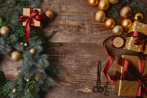 υπερυψωμένη θέα κουτιά δώρου Χριστουγέννων, fir στεφάνι, κορδέλα εκτύπωσης σε ουρά και ψαλίδι στο ξύλινο τραπέζι - Φωτογραφία, εικόνα
