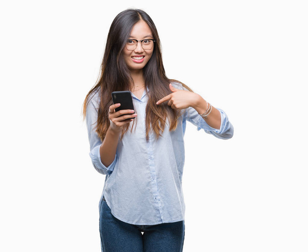 Young asian woman texting using smartphone over isolated background with surprise face pointing finger to himself - Valokuva, kuva