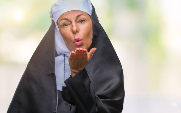 Seniorin christlich-katholische Nonne mittleren Alters mit isoliertem Hintergrund, die in die Kamera blickt und einen Kuss mit der Hand auf die Luft pustet, ist schön und sexy. Liebesausdruck. - Foto, Bild