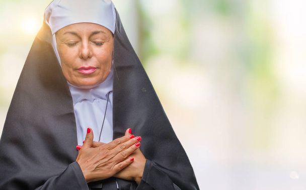 Średnim wieku starszy chrześcijańskiej zakonnica katolicka kobieta na białym tle uśmiechający się rękami na piersi z zamkniętymi oczami i wdzięczny gest na twarzy. Pojęcie zdrowia. - Zdjęcie, obraz
