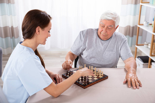 年配の男性は自宅とチェス若い女性世話人 - 写真・画像